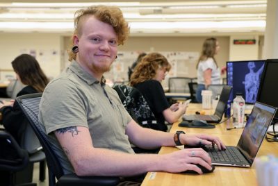 A student sits at a desk in front of an open laptop computer.