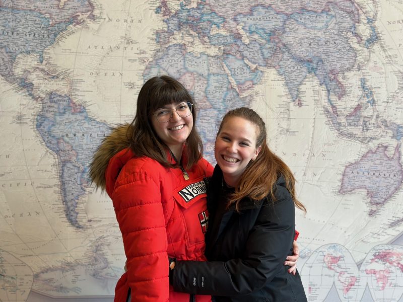Sara Alvarez Parejo and Marta Macario at the Virginia Tech Global Education Office lobby hugging and posing in front of a world map.